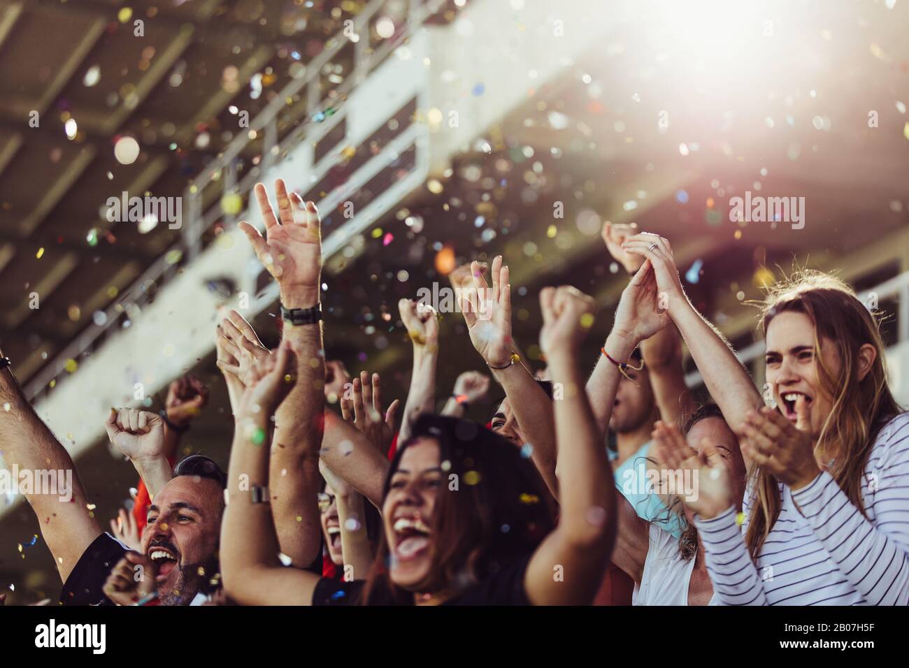 Sportfans klatschen mit herabfallendem Konfetti in die Hände. Fans der Fußballmannschaft jubeln im Stadion. Stockfoto