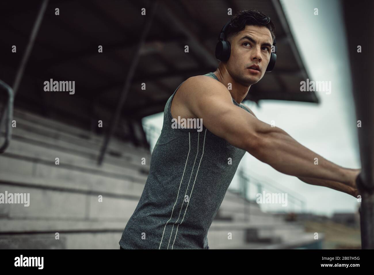 Passen Sie jungen Mann in Sportswear, der Kopfhörer trägt, um während des Trainings im Freien Musik zu hören. Sportlerin, die Pause vom Training und Musikhören am nimmt Stockfoto