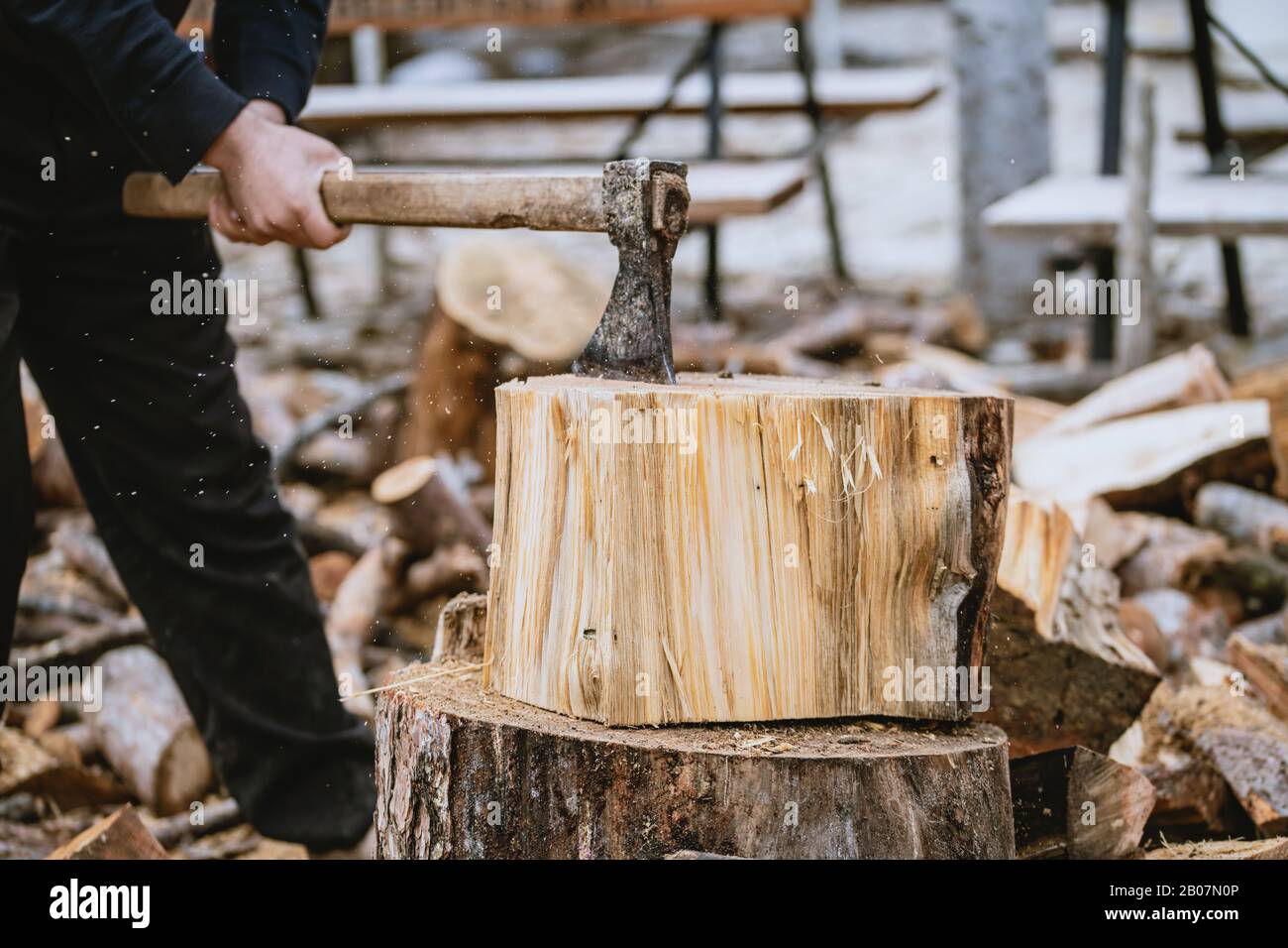 Mann hackt Holz mit Vintage-Axt. Details zu fliegenden Holzstücken auf Holzklotz mit Sägemehl. Stockfoto