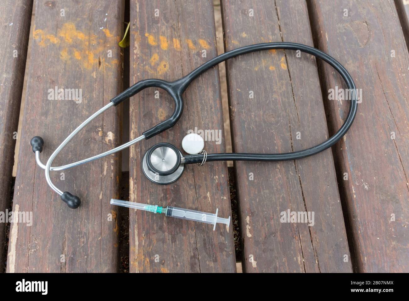 Nahaufnahme eines medizinischen Stethoskops neben einem Saringe und einer Nadel. Auf einem Holztisch Stockfoto