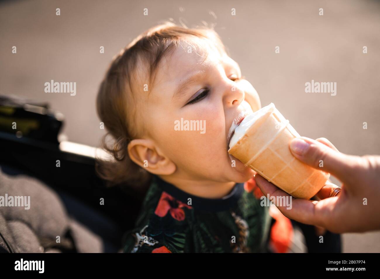Mutter füttert Baby Kind Junge Eiscreme - Junge Mutter und ihr Baby essen weißes Vanille cremig Dessert - Sitzt in einem Babywagen Kinderwagen - kaukasische Familie 1 Stockfoto