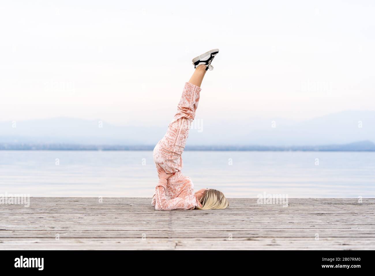 Eine schöne Frau führt die Übungen durch, die ihre Beine nach oben, See, Pier, Fitness anheben. Sport. Yoga. Stockfoto