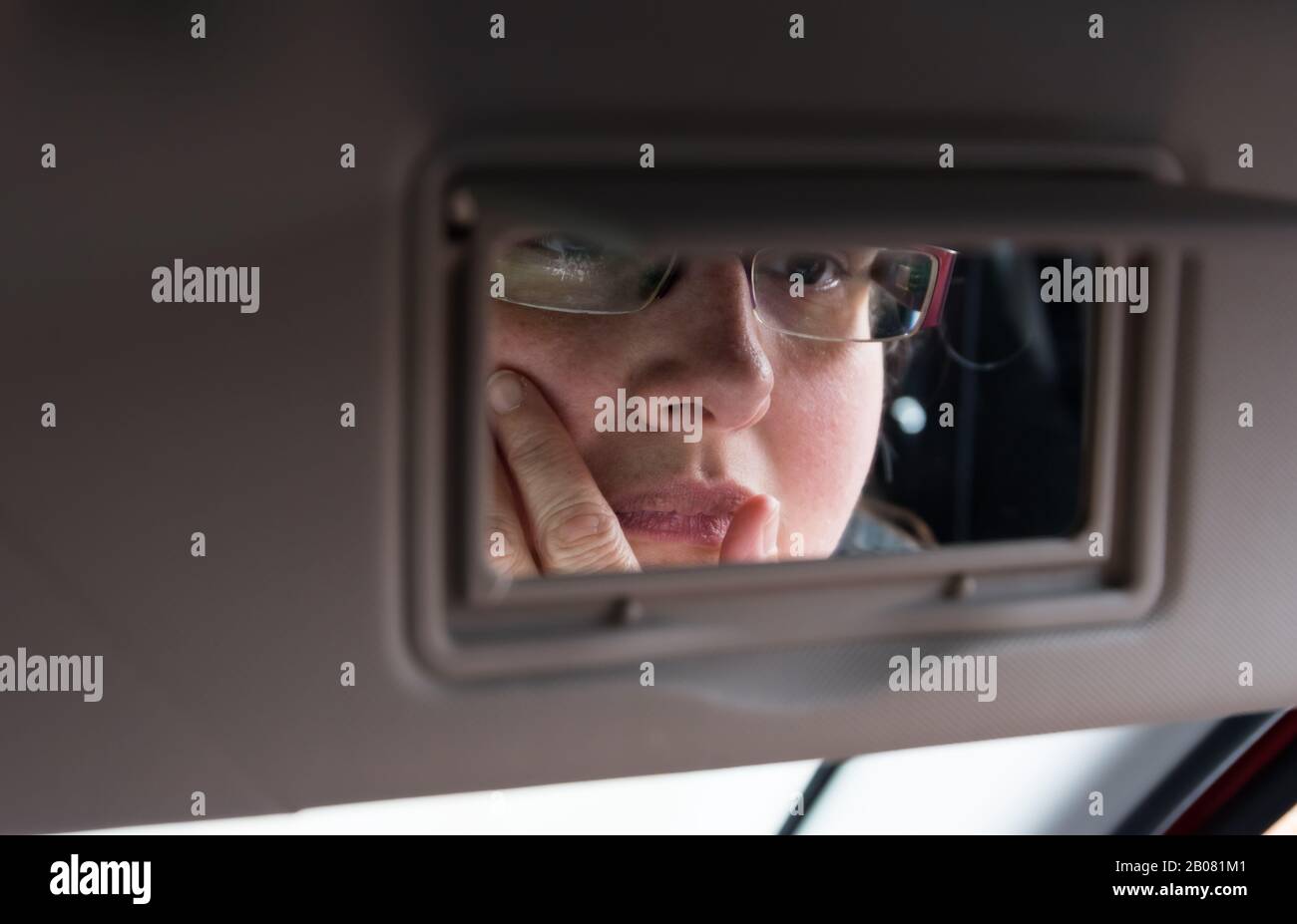 Selbstreflektion Konzept. Frau, die in einem Spiegel in der Sonnenblende eines Autos auf sich selbst blickt und denkt. Denkzeitkonzept. Konzept der Selbstreflexion. Stockfoto
