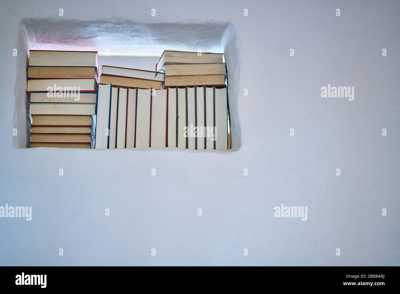Helle und sonnige Details von Stapeln von Büchern in einem Raum in einer texturierten weißen Wand, Kopierraum und niedrigem Winkel Stockfoto