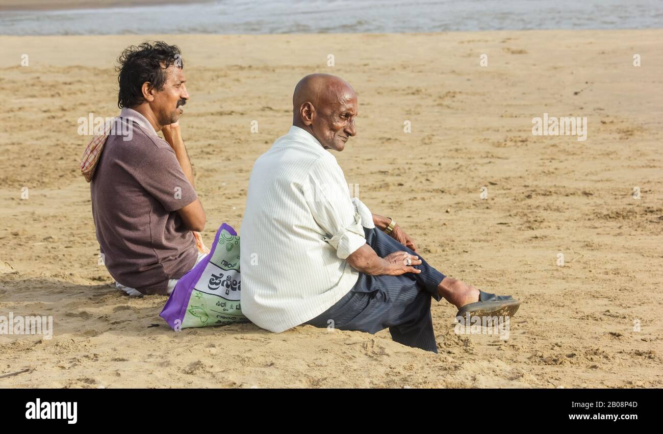 Zwei indische Männer sitzen am Strand von Gokarna und starren auf den Ozean. Stockfoto