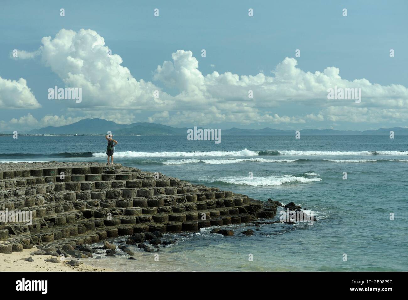 Frau, die auf Betonblock-Wellenbrecher steht und auf das Meer blickt. Lombok, Indonesien Stockfoto