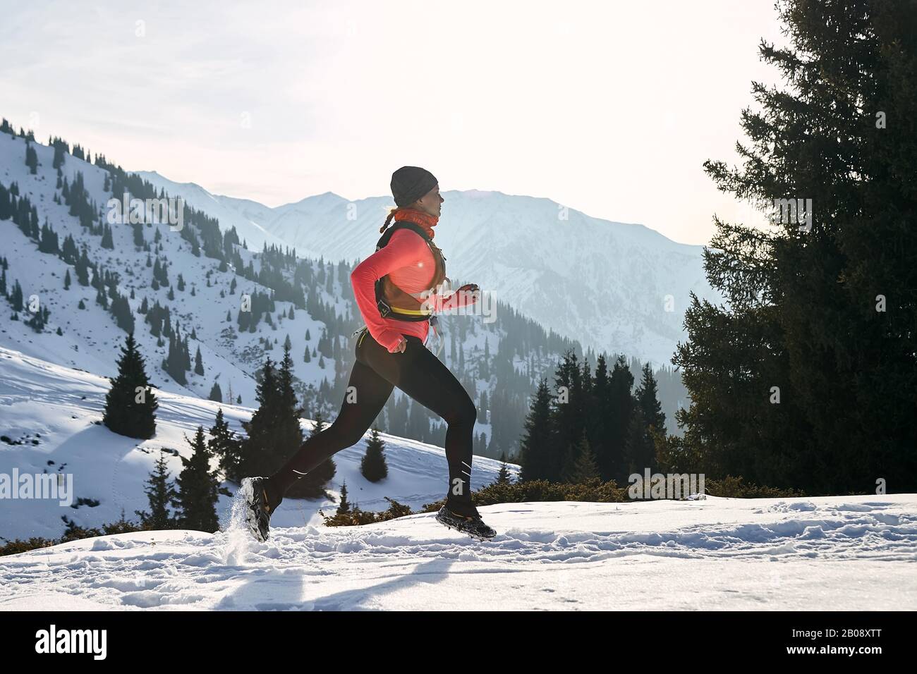 Der Trailrunner in pinkfarbener Jacke, Frau, die im Winter in den Bergen unterwegs ist, ist auf Schnee. Stockfoto