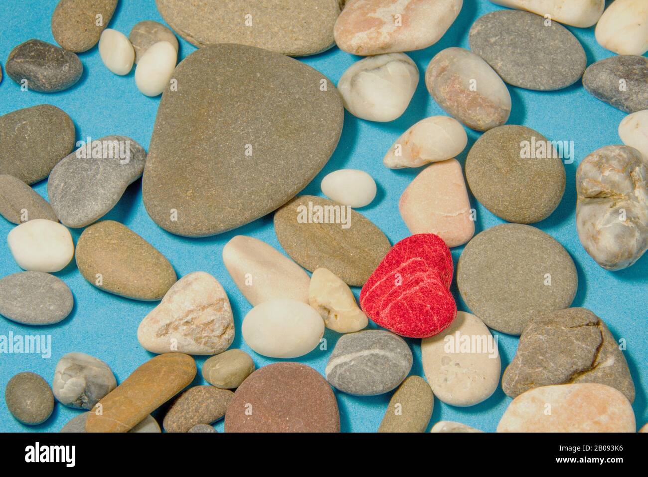 Roter, herzförmiger Stein auf blauem Grund mit farbenfrohen Meeressteinchen Stockfoto