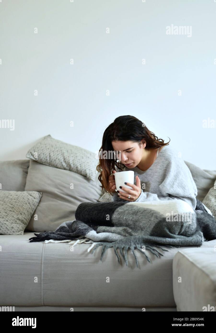 Das junge Mädchen trinkt Tee auf einem grauen Sofa Stockfoto