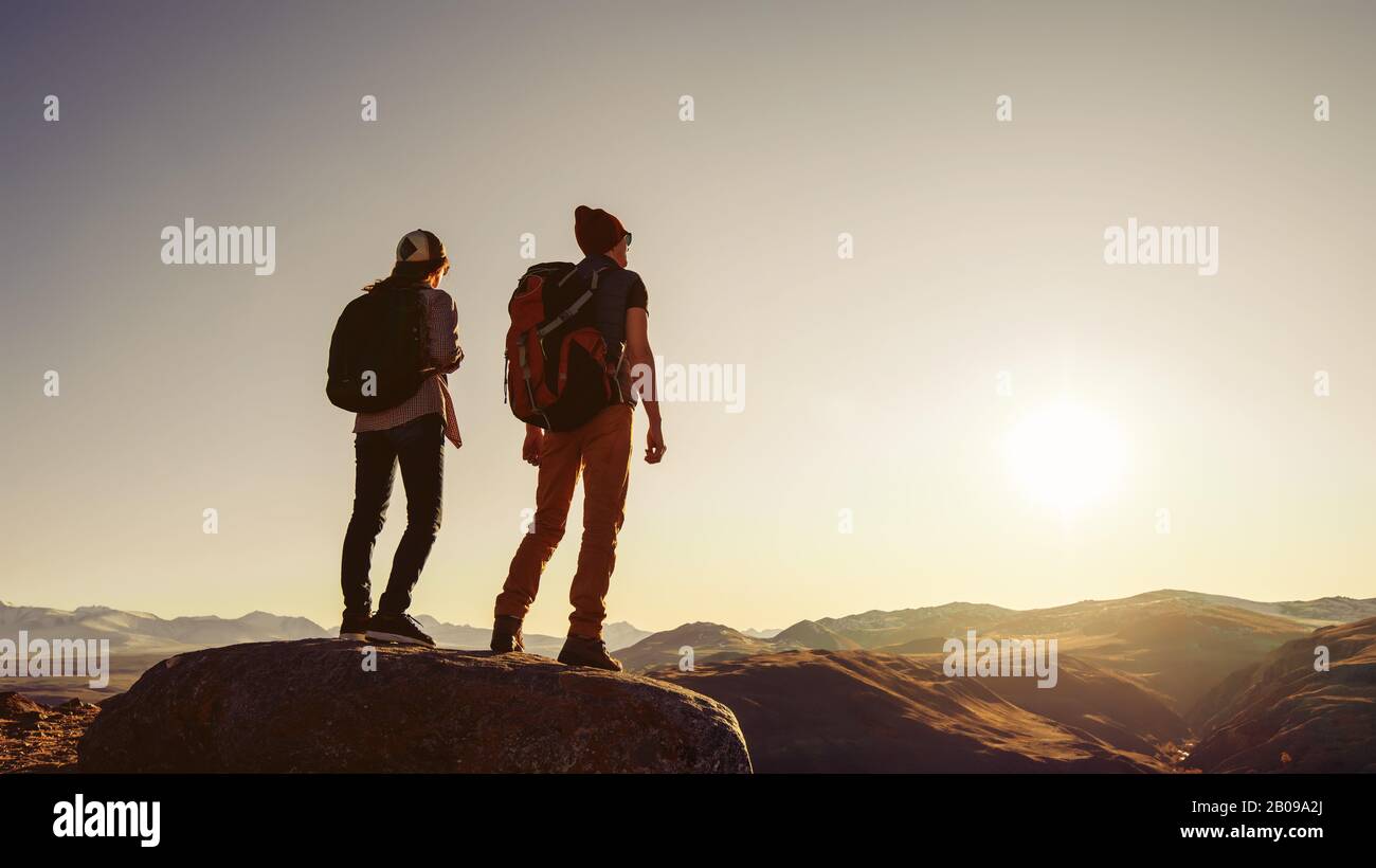 Zwei Reisende oder Wanderer stehen bei Sonnenuntergang auf einem großen Felsen in der Berggegend Stockfoto