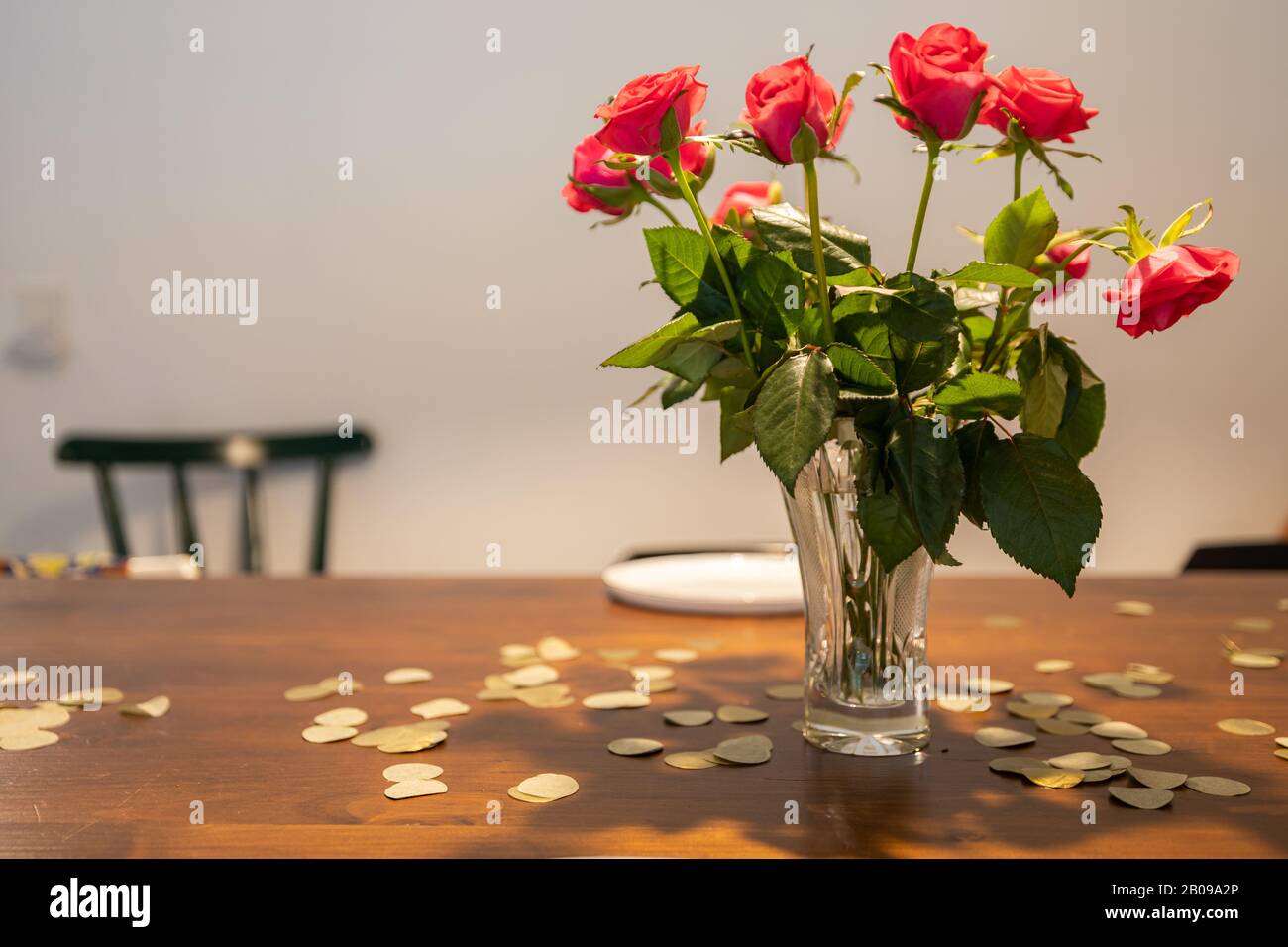 Vase mit roten Rosen auf einem Tisch mit goldenem Konfetti. Stockfoto