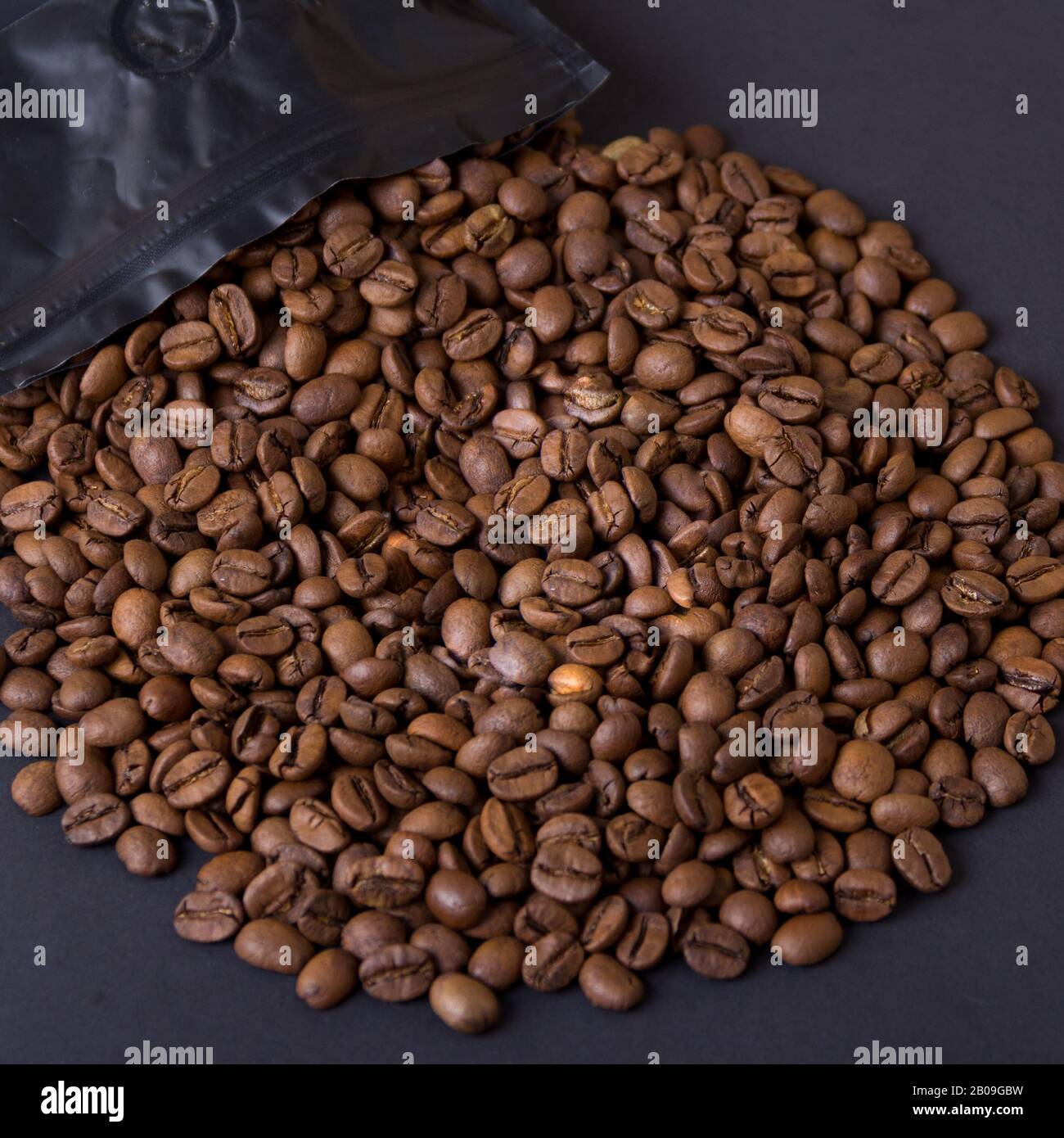 Kaffeebohnen verschütten sich aus einer schwarzen Packung. Kaffee-Hintergrund. Stockfoto