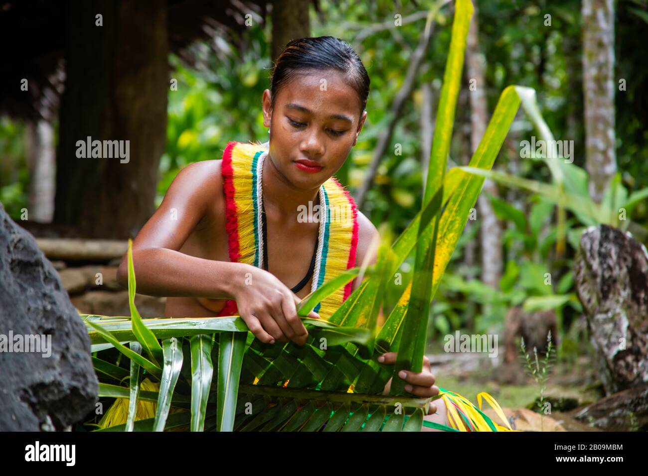 Diese junge Frau (MR) ist in einem traditionellen Outfit für kulturelle Cerimonies und webt einen Korb aus einer Palmfront auf der Insel Yap, Mikronesien. Stockfoto