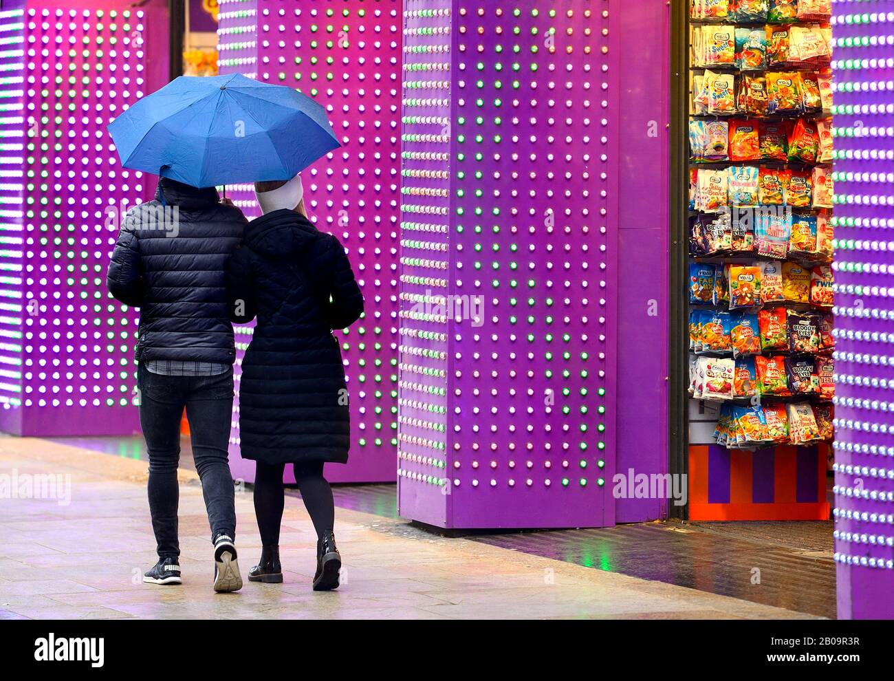 London, England, Großbritannien. Ein Paar, das an einem regnerischen Tag am Kingdom Of Sweets im Piccadilly Circus vorbeiläuft Stockfoto