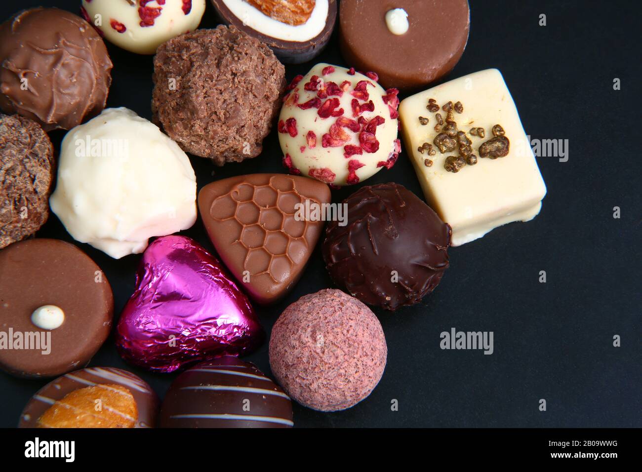 Nahaufnahme einer Auswahl an Luxus-Pralinen mit einer Folie, die mit rosafarbenem Herzen umhüllt ist und für ein Geschenk sein könnte. Stockfoto