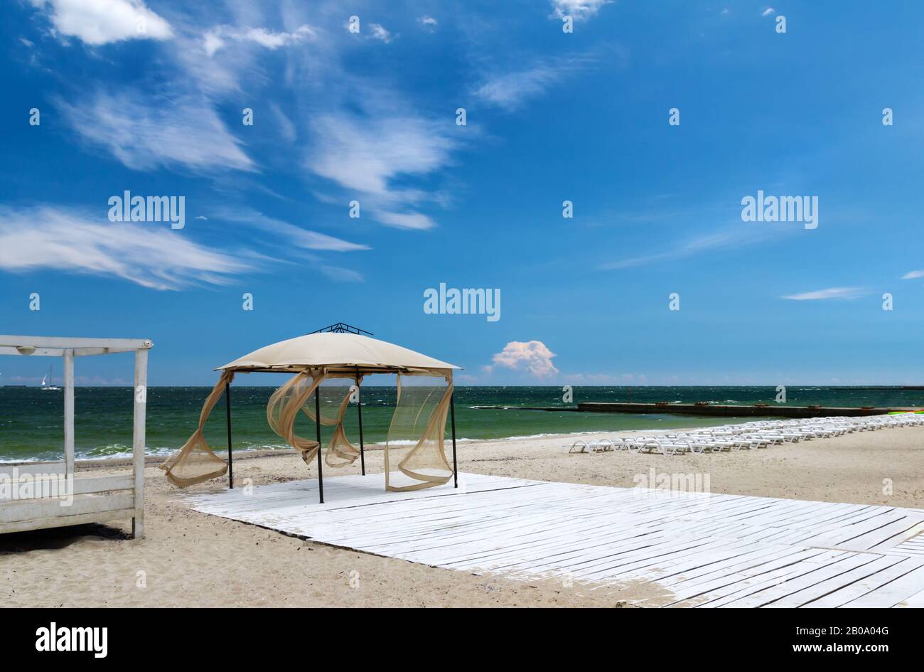 Sommer, duftige Sonne, windige Wetterlage, eingelassene Strände mit Sonnenpavillon und leeren Sonnenliegen. Blauer Himmel auf dem Hintergrund Stockfoto