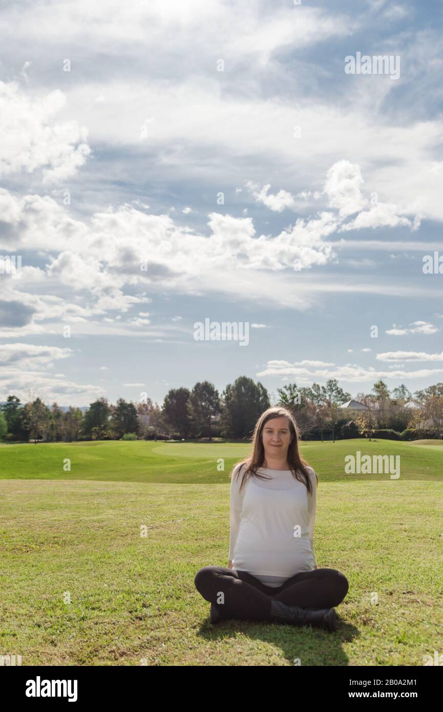 Schwangere 30 Jahre alte Frau, die im Nest mit natürlicher Landschaft im Hintergrund posiert Stockfoto