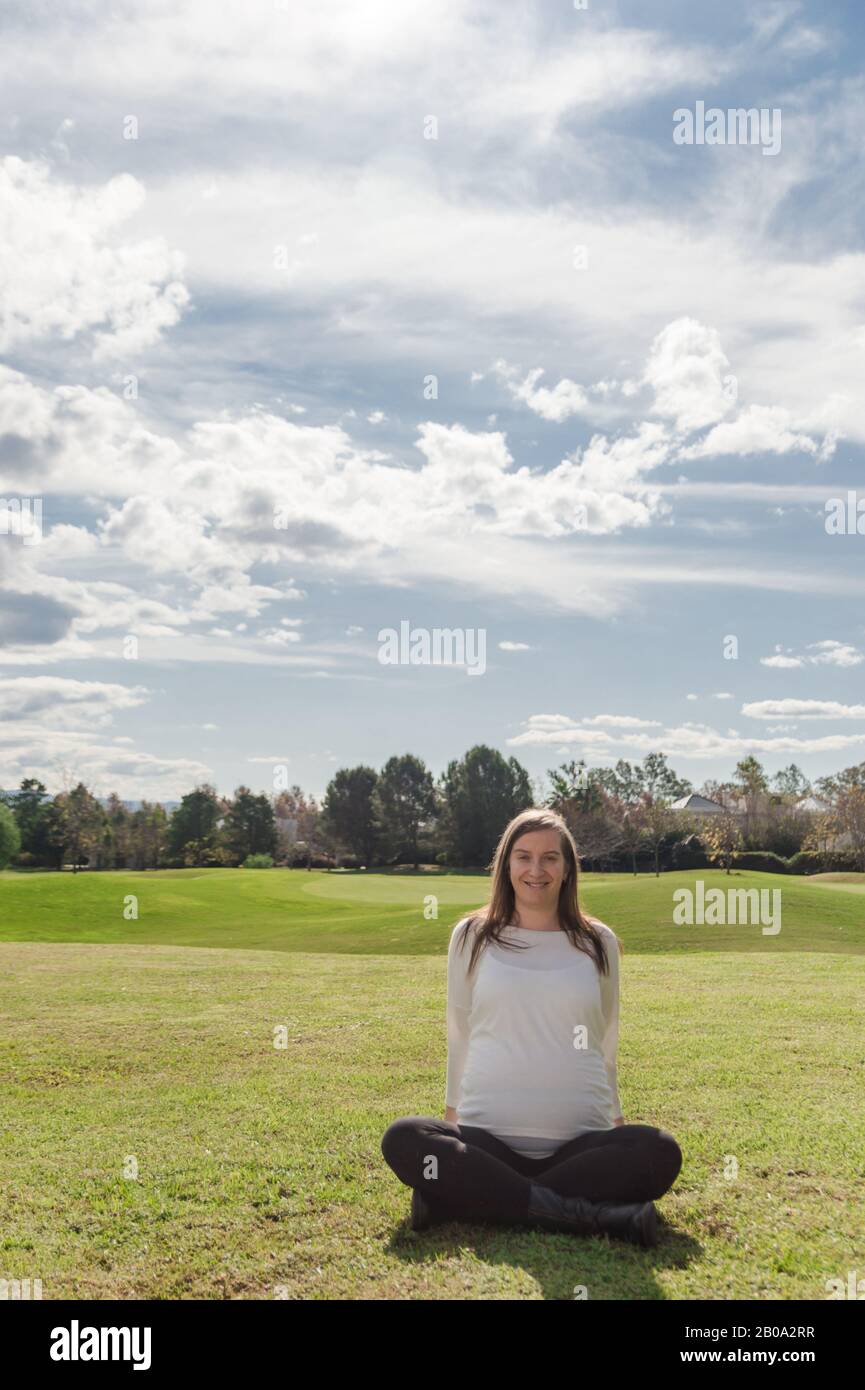 Schwangere 30 Jahre alte Frau, die im Nest mit natürlicher Landschaft im Hintergrund posiert Stockfoto