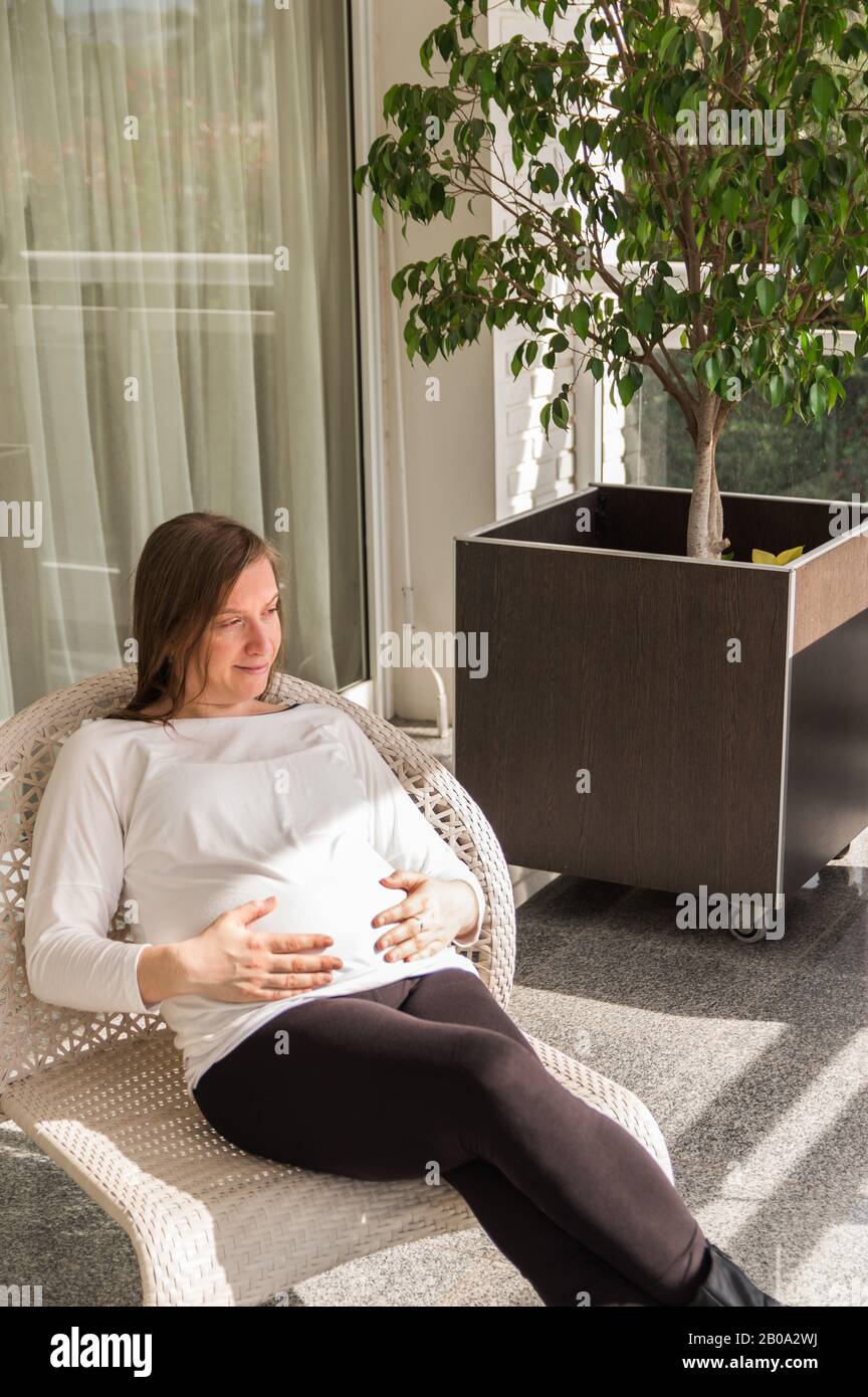 Schwangere 30-jährige Frau posiert in einem Sessel in einer Galerie Stockfoto