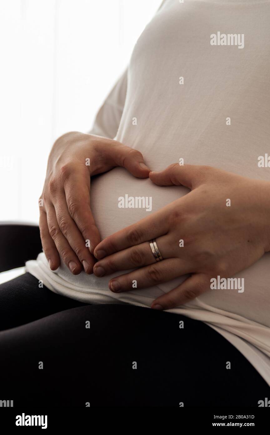 Schwangere 30-jährige Frau mit herzförmigen Händen auf ihrem schwangeren Bauch Stockfoto
