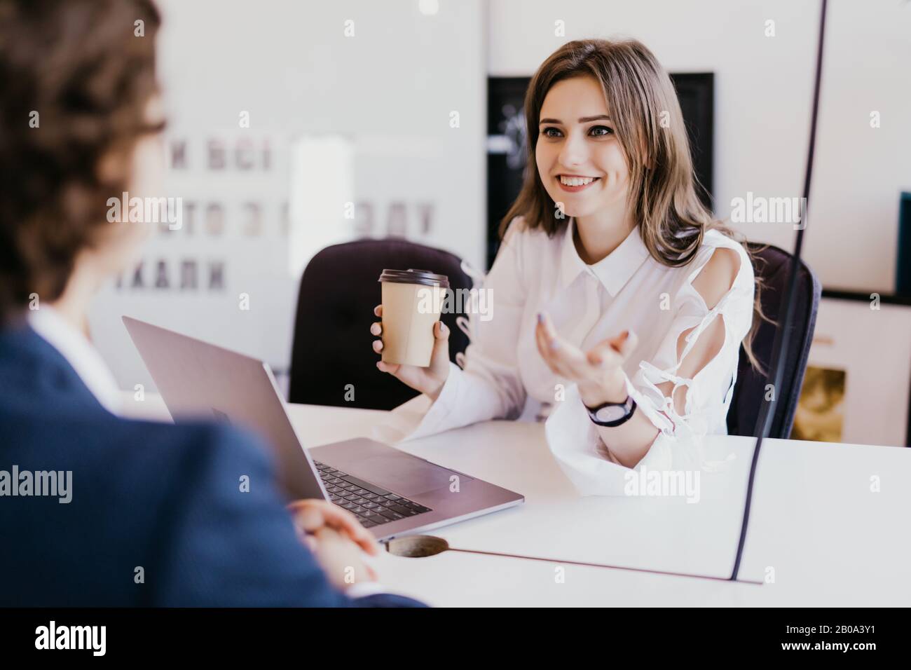 Geschäftspaar in legerer Kleidung verwendet einen Laptop, diskutiert über Angelegenheiten, trinkt Kaffee und lächelt während der Arbeit im Büro Stockfoto
