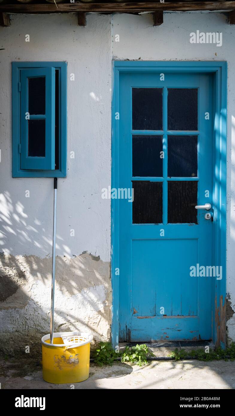 Traditioneller Eingang im zyprischen Haus mit blau geschlossener Tür, offenem Fenster und einem gelben Mopp Stockfoto