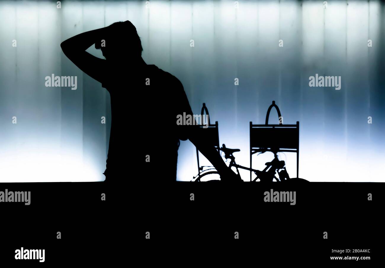 Silhouetten eines ängstlichen jungen Mannes, der in der Nacht vor einem modernen Gebäude in hohem Kontrast zwischen Schwarz und Blau weiß spazieren geht Stockfoto