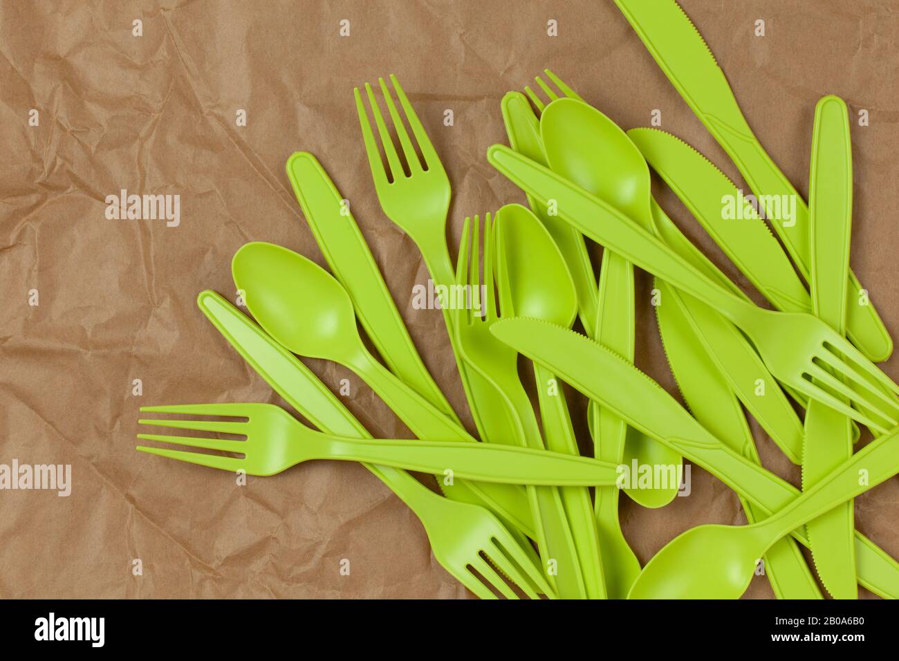 Hintergrund aus wiederverwendbaren, recycelbaren grünen Gabeln, Löffeln, Messern aus Maisstärke auf braun zerknittertem Fertigungspapier. ECO, kein Abfall, Alternative zu p Stockfoto