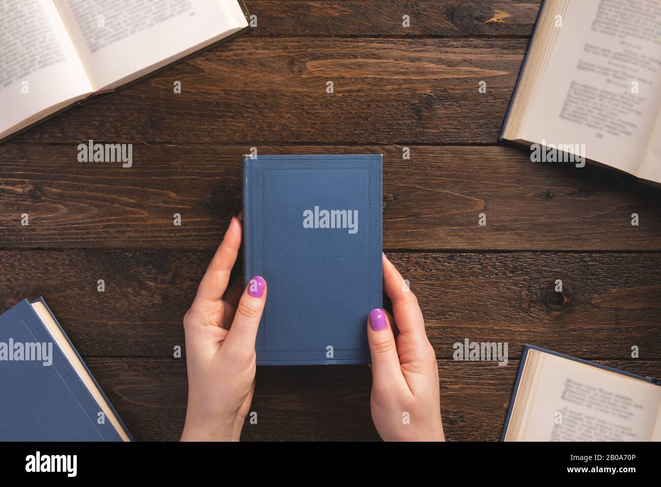 Weibliche Hände mit altem Buch. Bücher auf Holzhintergrund. Flaches Layout, Draufsicht, Kopierbereich. Stockfoto
