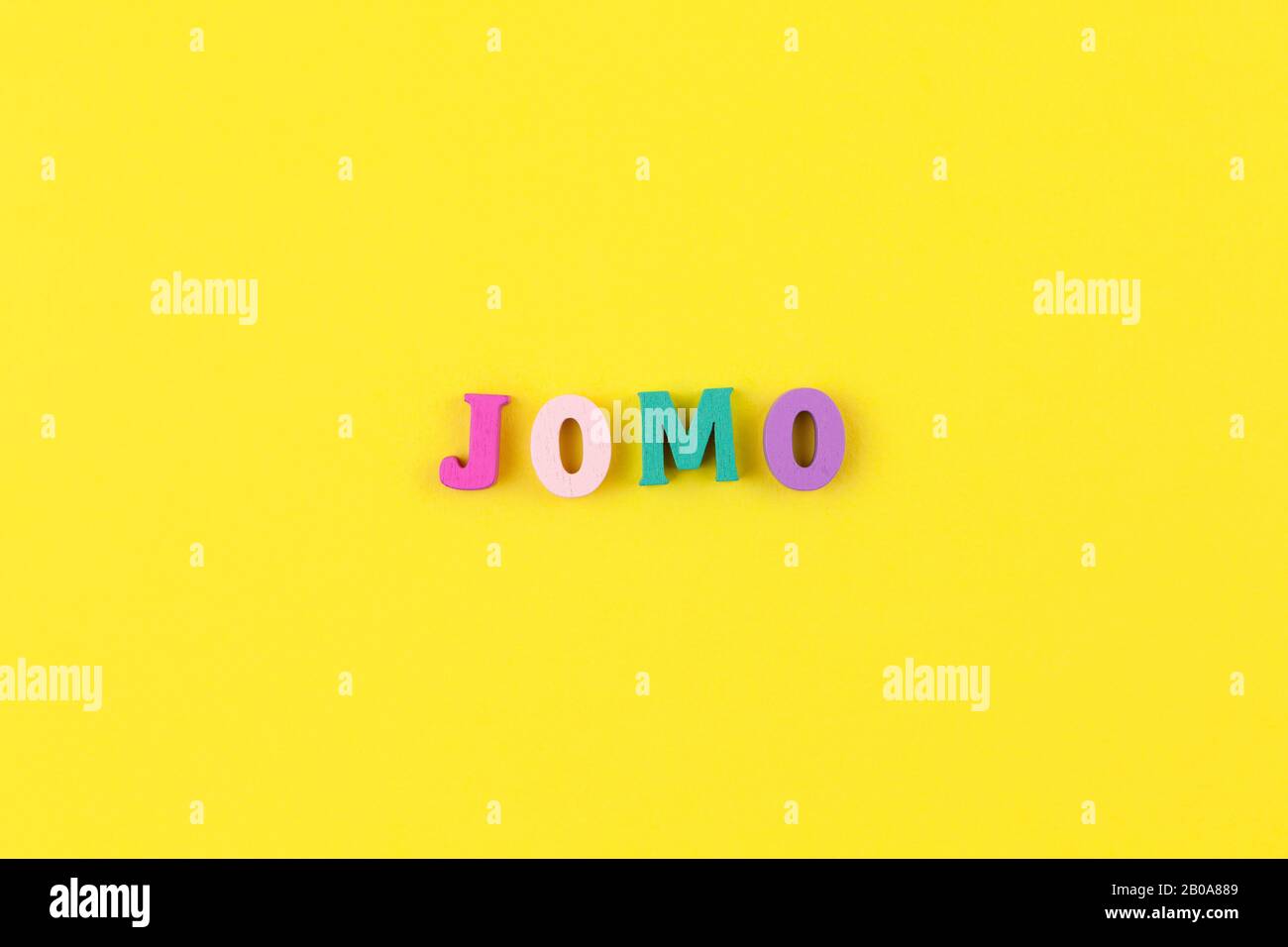 Abkürzung Wort JOMO in bunten Buchstaben auf Holz Pastell gelben Hintergrund. JOMO - Freude fehlt. Opposition, Wahl, soziale Problem, digi Stockfoto