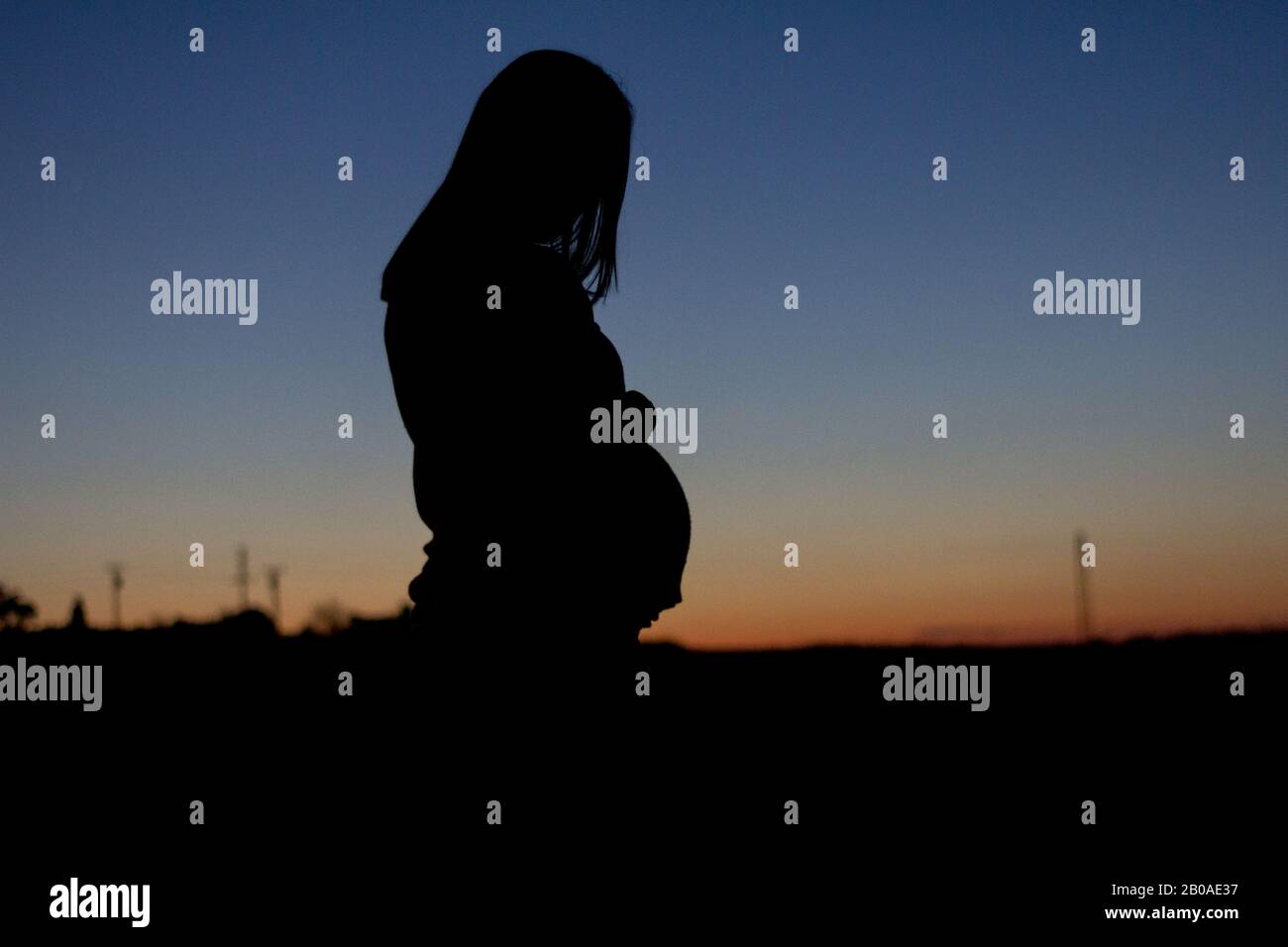 Eine schwangere Frau wird gegen einen bunten Sonnenuntergang silhouetted Stockfoto