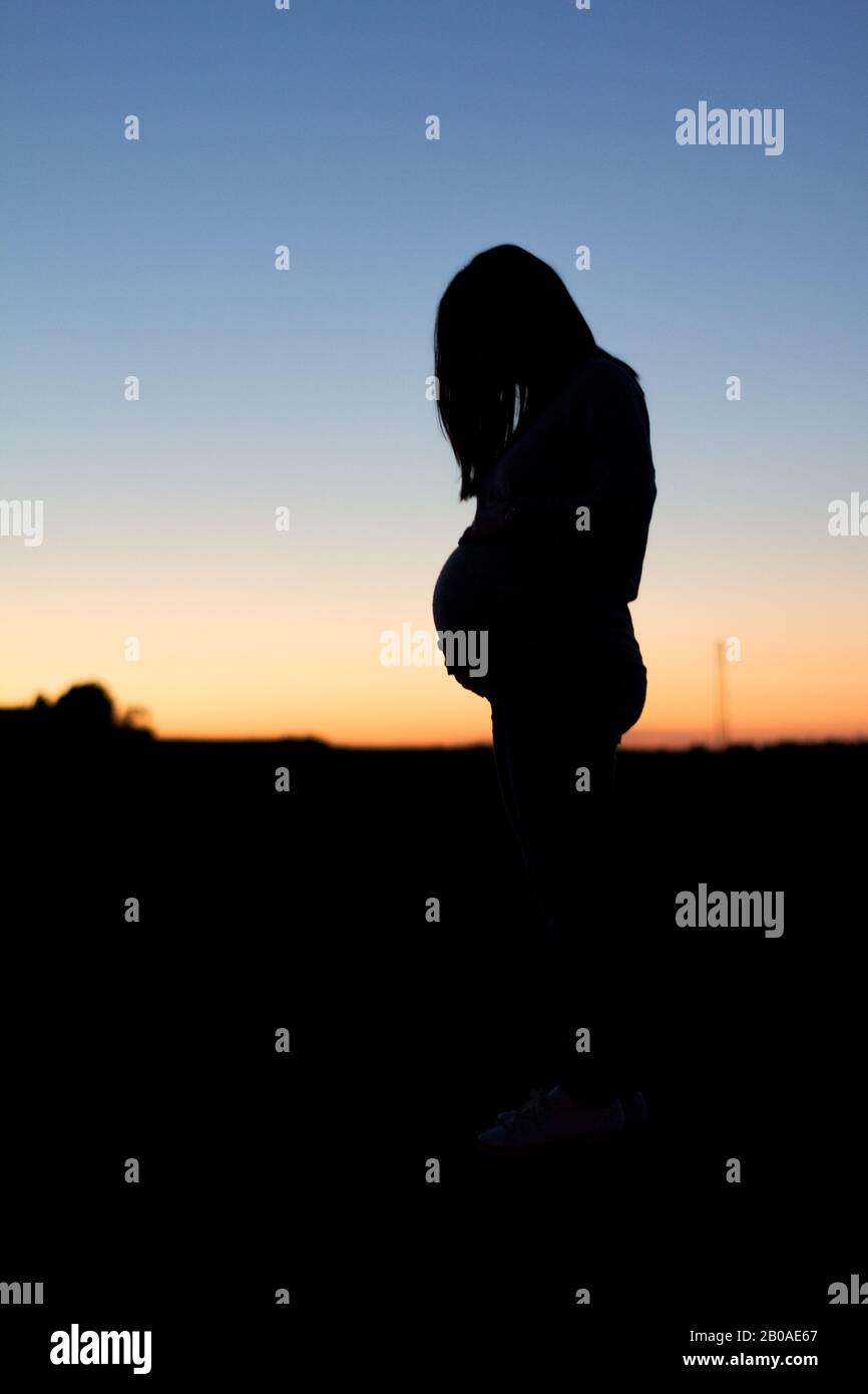 Eine schwangere Frau wird gegen einen bunten Sonnenuntergang silhouetted Stockfoto