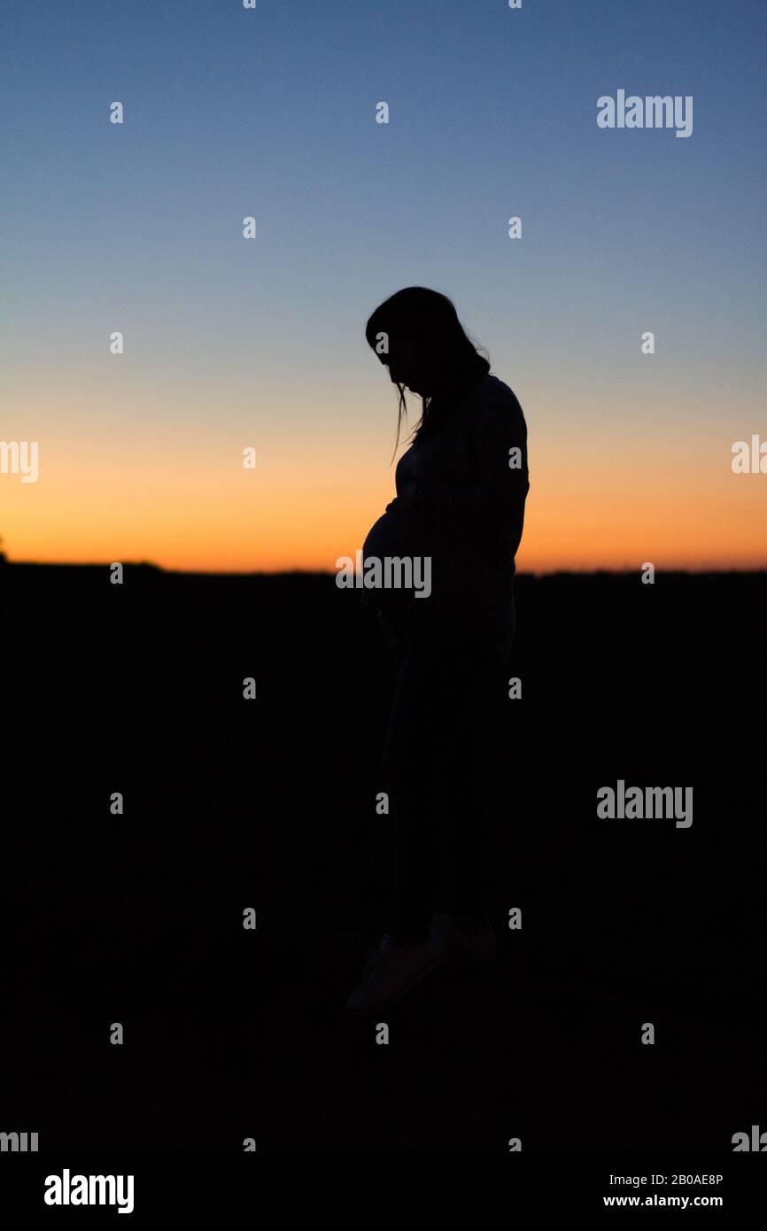 Eine schwangere Frau ist halb gegen einen bunten Sonnenuntergang silhouetted Stockfoto