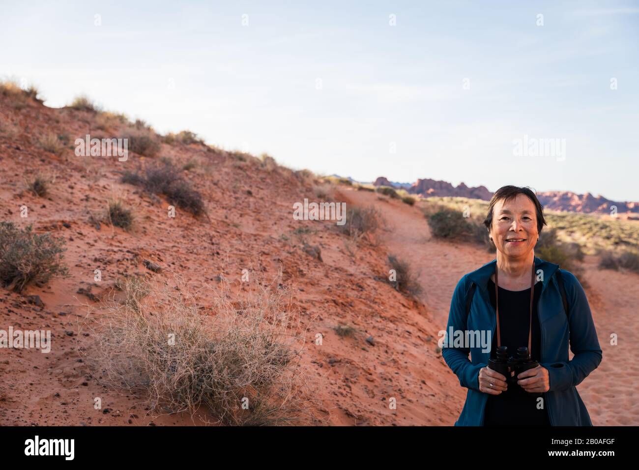 Ältere asiatische Frau lächelt mit Fernglas in der Wüstenlandschaft Stockfoto