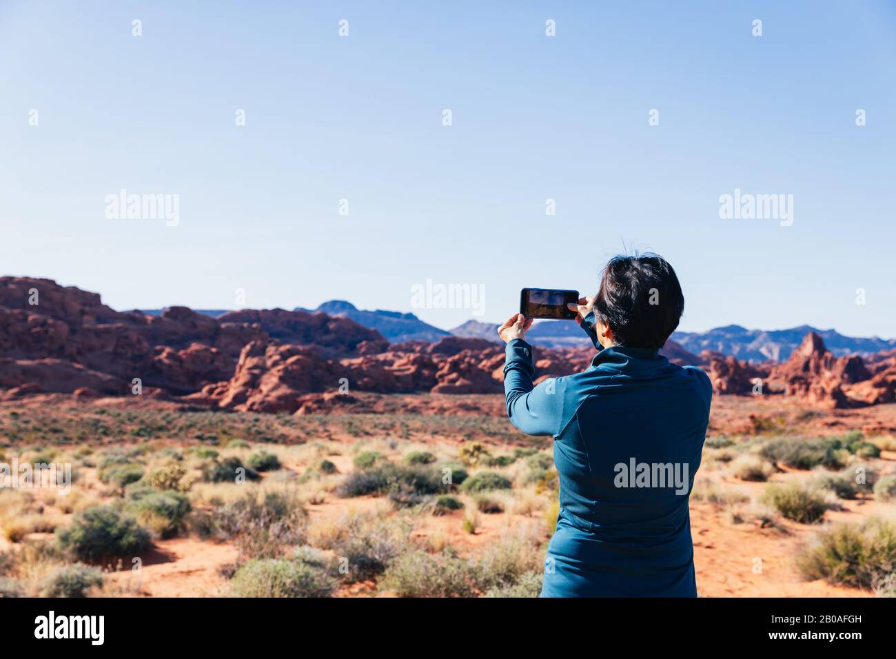 Ältere asiatische Frau, die mit ihrer Kamera ein Foto von einer Wüstenlandschaft fotografiert Stockfoto