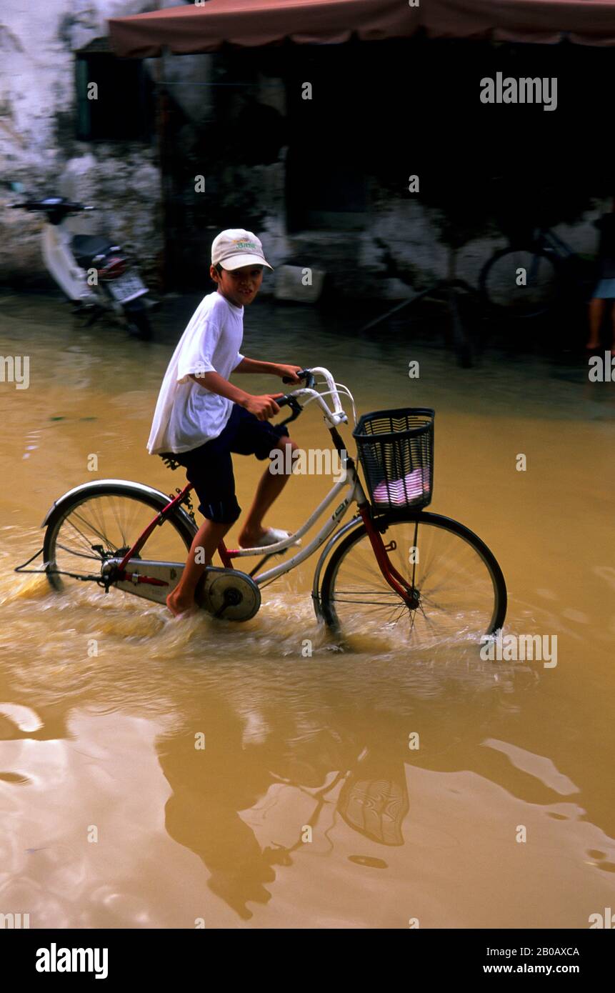 VIETNAM, HOI AN, STRASSENSZENE, ÜBERSCHWEMMTE STRASSEN NACH STARKEM REGEN, JUNGE AUF DEM FAHRRAD Stockfoto