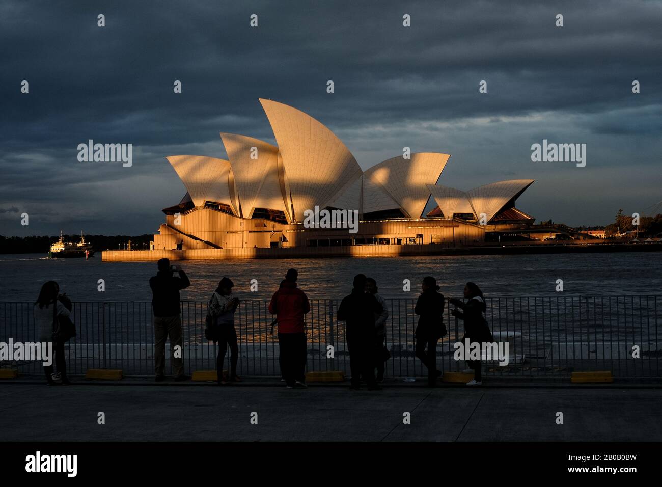 Eine Reihe von Touristen in Campbells Cove fotografiert das Sydney Opera House in goldenem Sonnenlicht und Schattenlinien, die von der Harbour Bridge geworfen werden Stockfoto