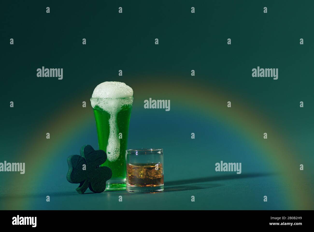 St. Patrick's Pint Bier und Irish Whiskey mit Wood Four Leaf Clover auf grünem Hintergrund und Rainbow Stockfoto