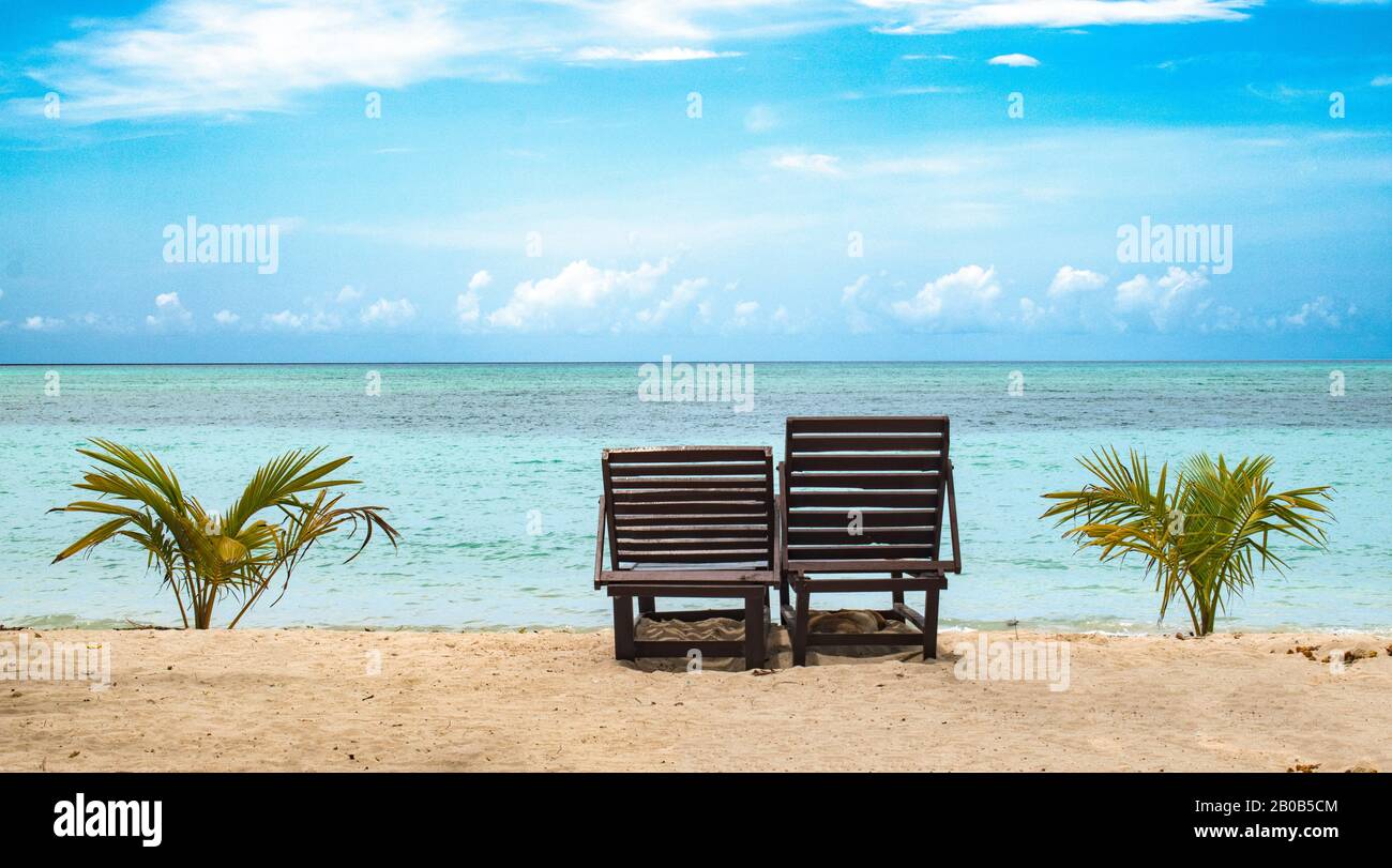 Wunderschönes Foto von zwei Holz-Ruhesesseln, die für Touristen und Flitterwochen-Paare am Strand frei sind, um gute Zeiten zu verbringen. Ruhiges türkisfarbenes Meer Stockfoto