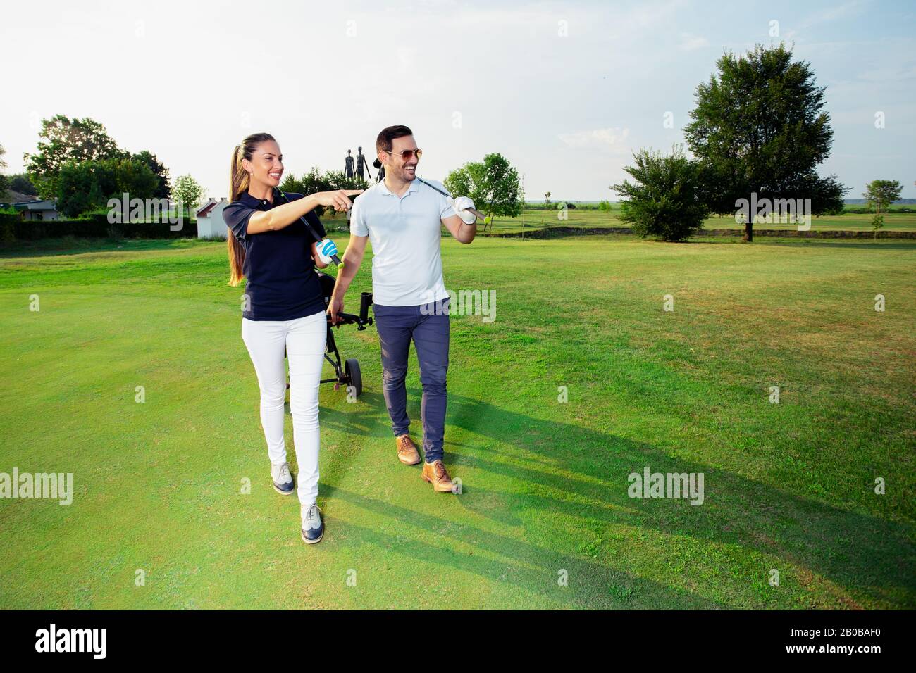 Schöner weiblicher Golfspieler und gutaussehender männlicher Spieler laufen auf einem Golfplatz. Stockfoto