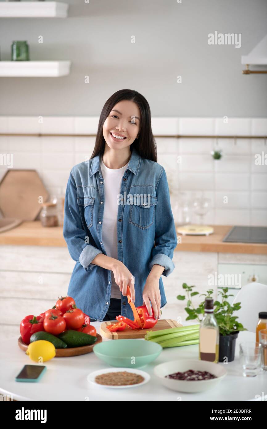 Junges Mädchen, das in der Nähe des Küchentischs steht und Paprika zerschneiden kann. Stockfoto