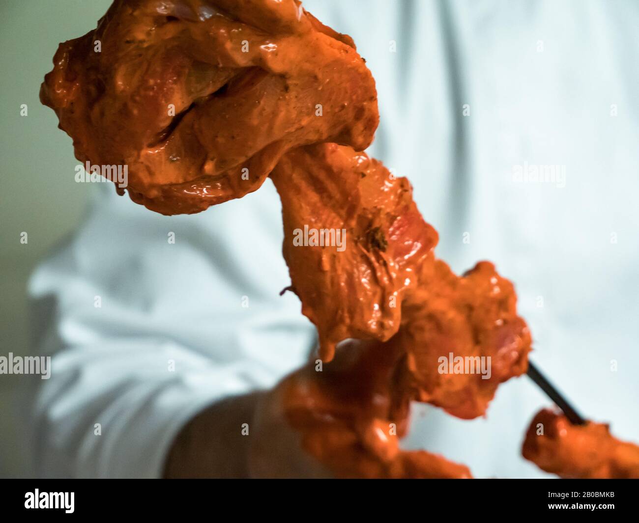 Ein indischer Koch schiebt mariniertes Huhn auf einen langen Metallküchespieß, der für eine Tandoori-Küche bereit ist. Stockfoto
