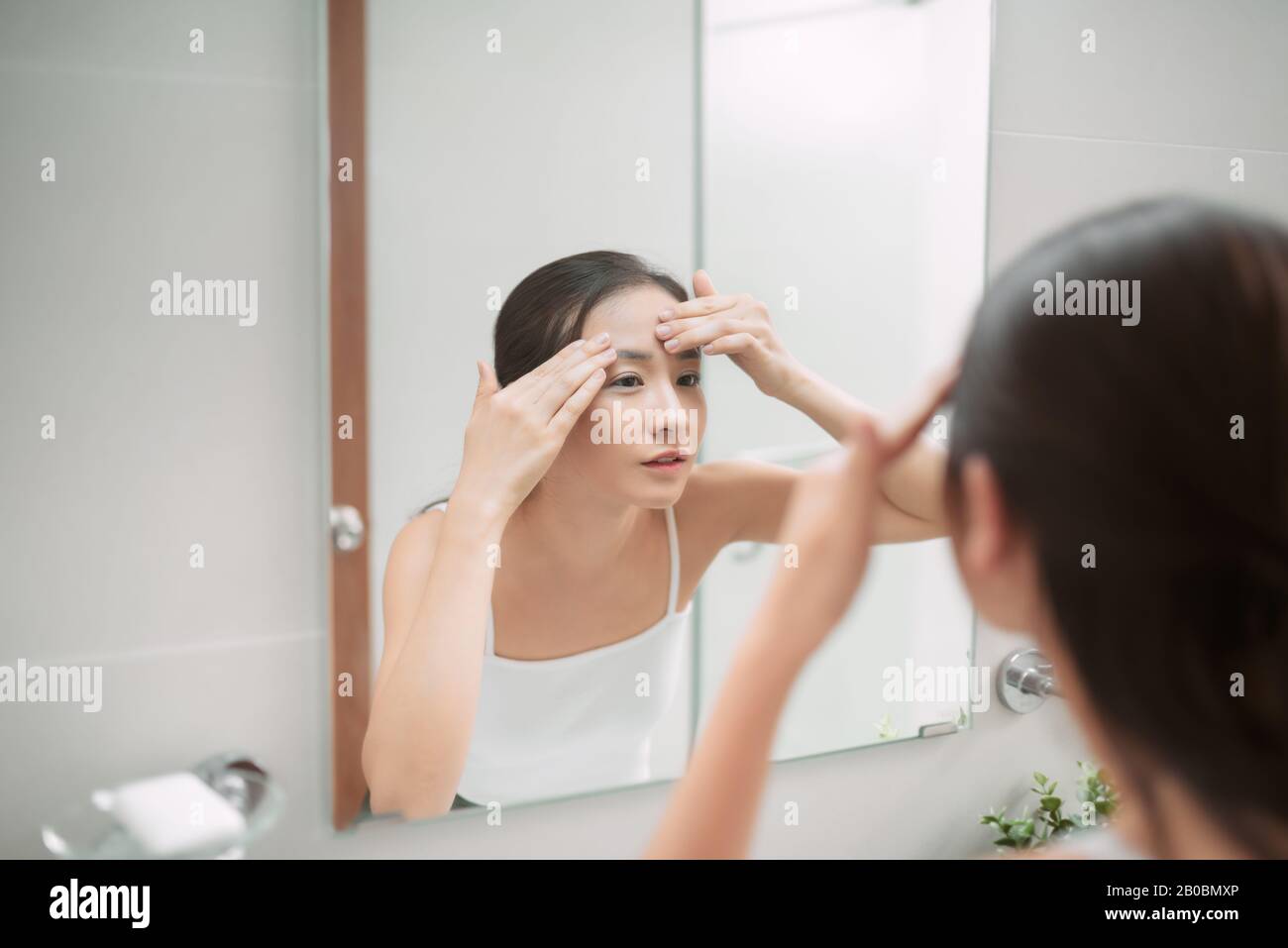 Schönheit in Spiegelreflexion. Über der Schulter des Gesichts einer schönen Frau, die ihr Gesicht berührt, während sie in den Spiegel schaut Stockfoto