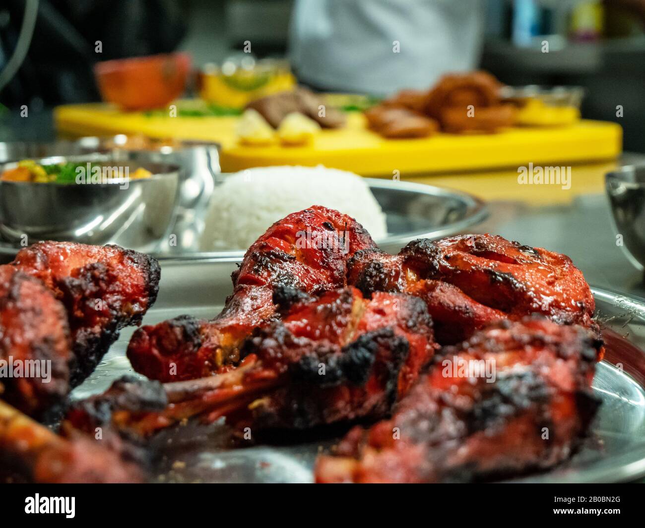 Nahaufnahme eines Tellers gekochtes Tandoori-Hähnchen im Vordergrund mit Reis und anderen indischen Speisen im Hintergrund. Stockfoto