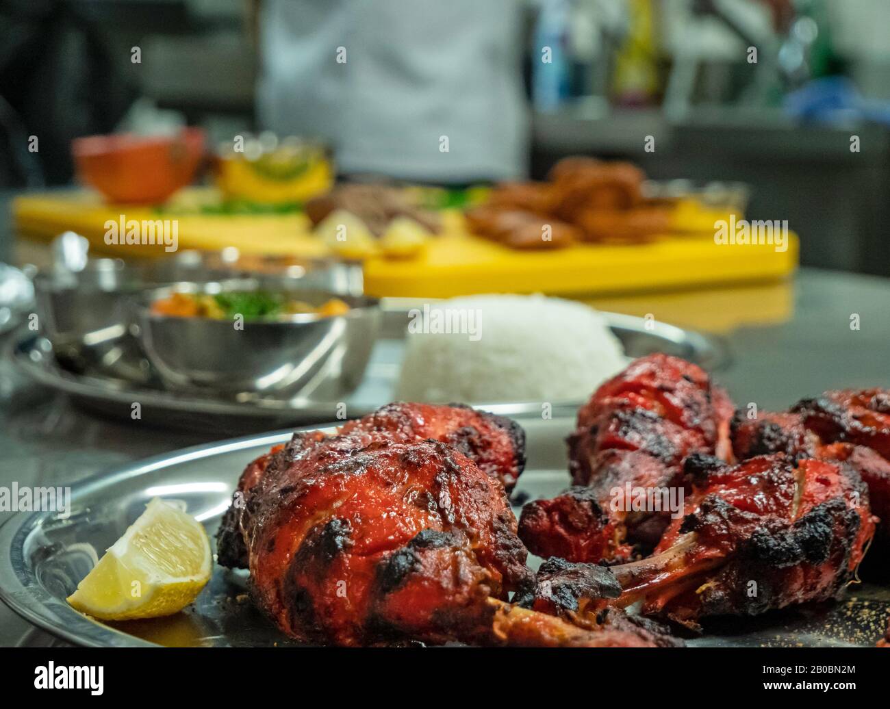 Nahaufnahme eines Tellers gekochtes Tandoori-Hähnchen im Vordergrund mit Reis und anderen indischen Speisen im Hintergrund. Stockfoto