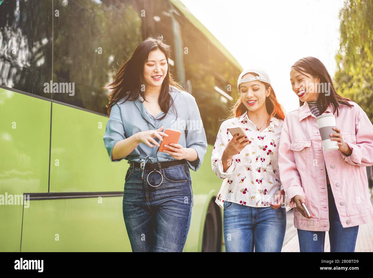 Fröhliche asiatische Freunde, die Smartphones am Busbahnhof nutzen - Junge Studenten, die sich nach der Schule im Freien über Technologietrends lustig machen - Freundschaft, Univ Stockfoto