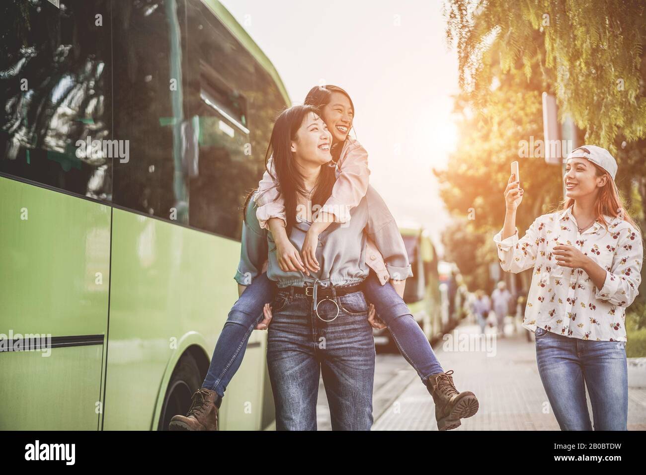 Fröhliche asiatische Freunde machen selfie-fotos mit Smartphones am Busbahnhof - Junge Studenten, die sich mit Technologietrends lustig machen - Freundschaft, Unive Stockfoto