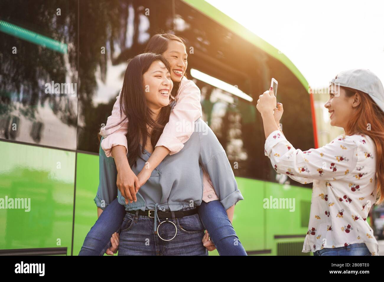 Fröhliche asiatische Studenten, die am Busbahnhof mit Smartphones Videos machen - Junge Leute haben Spaß an Technologietrends - Freundschaft, Universität und Trans Stockfoto
