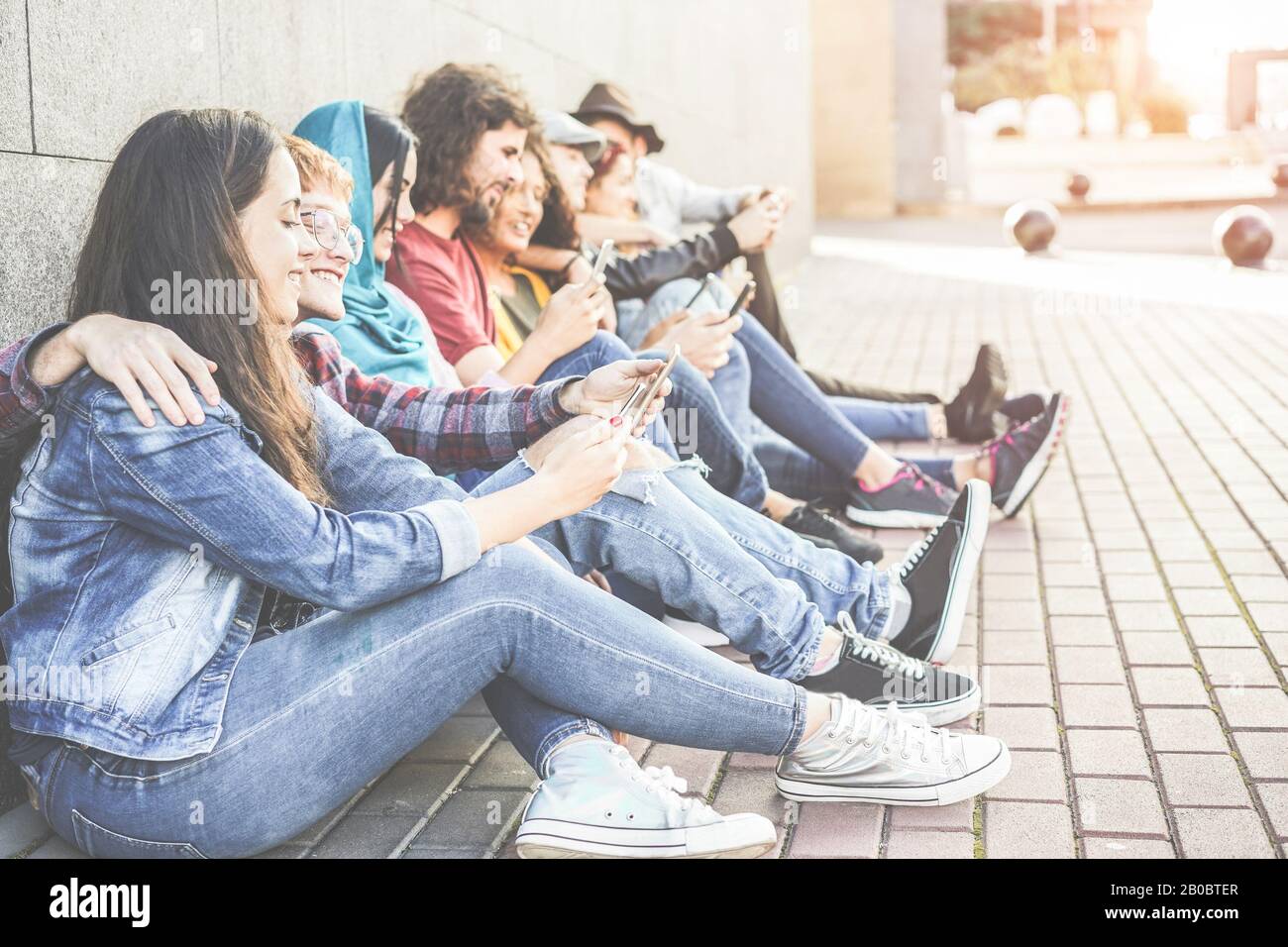 Tausendjährige Freunde, die im Freien sitzende Smartphones nutzen - Vielfältige Kultur Menschen sind auf neue Technologietrends eingestellt - Konzept der Jugend, sozialer Lebensstil Stockfoto