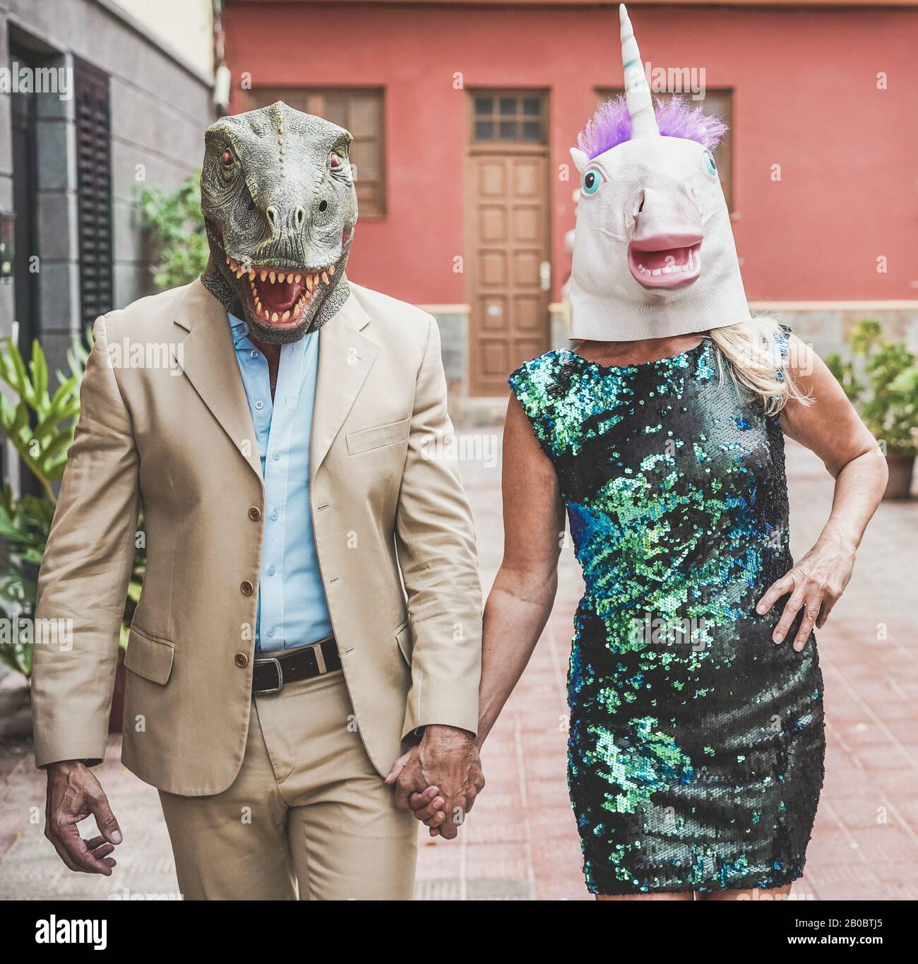 Verrücktes Senioren-Paar mit T-rex und Hähnchenmaske durch die Stadtstraße spazieren - Alte Trend-Leute, die zusammen Spaß haben - Absurdes und lustiges Trend-Konzept Stockfoto
